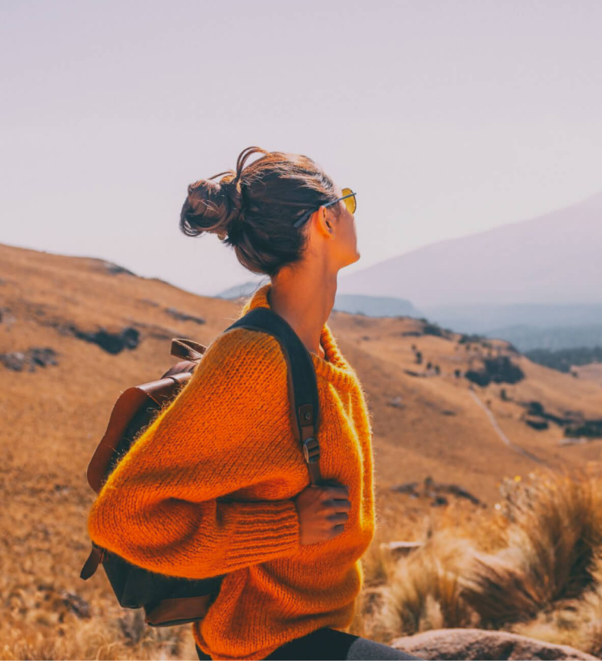 Traveler in an orange sweater looking out over golden hills
